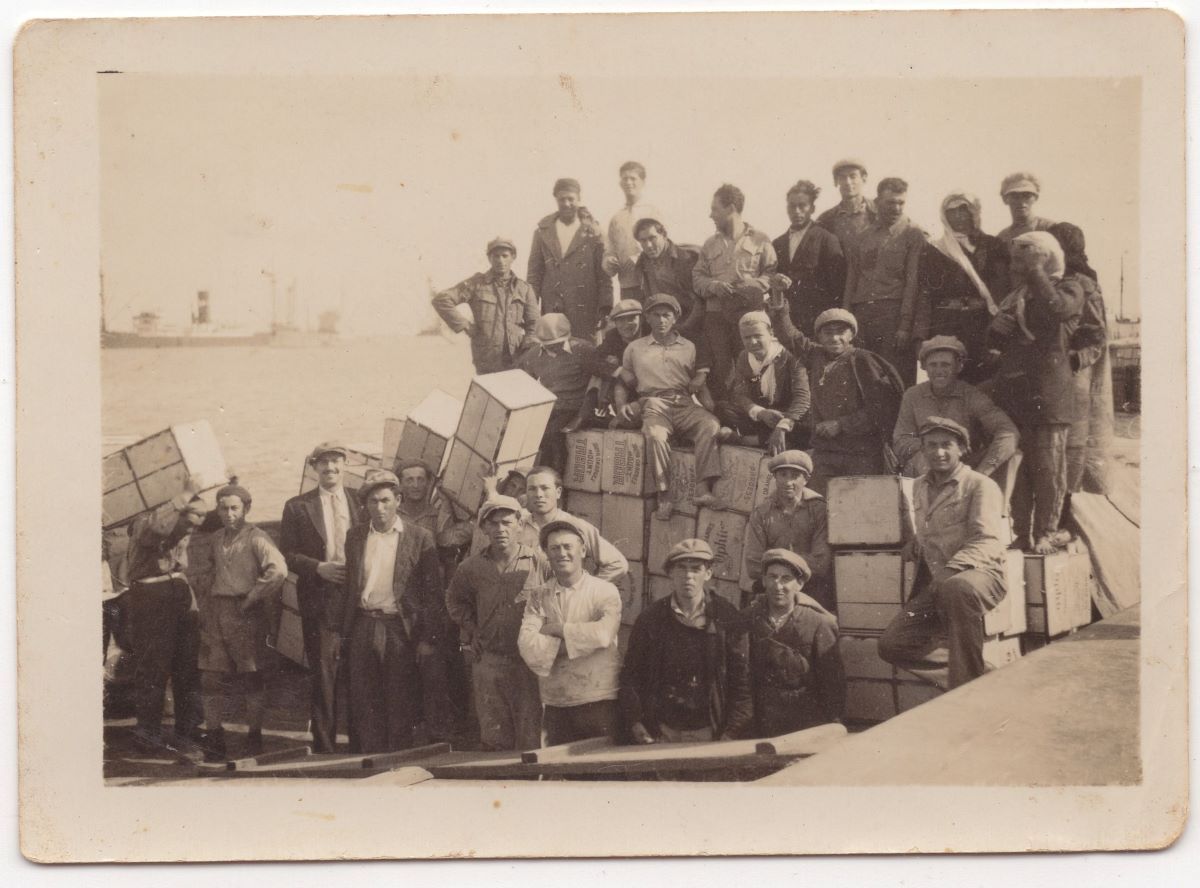 Grupė vyrų su Jafa apelsinų dežėmis. Jafos uostas. Asmeninė Anat Rosen kolekcija.